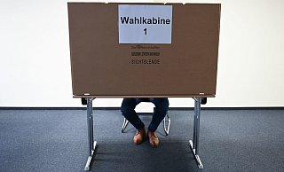 Ein Mann sitzt im Wahlraum des Briefwahllokals Frankfurt Innenstadt hinter einer Wahlkabine. - Foto: Arne Dedert/dpa