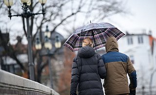 Spaziergänger laufen mit Schirm über eine Brücke in Hamburg. - Jonas Walzberg/dpa
