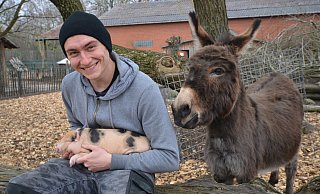 So könnte es mal aussehen: Tierpfleger-Azubi Marcel Ibers krault ein Minischwein-Ferkel - und Eseldame Mia schaut zu. - Birgit Vredenburg