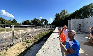 Clyde White (TG Werste) und Stefanie Dietrich (Muwis Sportvielfalt) schauen zusammen mit Stadtmitarbeiter Tino Müller über eine Außenwand des Umkleidegebäudes und träumen sich auf die neue Rundbahn. Die allerdings ist momentan eher Weide- als Sportland. - Nicole Sielermann