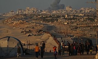 Vertriebene Palästinenser gehen entlang der Küstenstraße, während im Hintergrund Rauch nach einem israelischen Militärschlag in Gaza aufsteigt. - Abdel Kareem Hana/AP/dpa