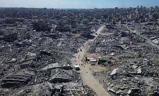 Auf diesem Drohnenfoto gehen Palästinenser eine Straße entlang, die von Gebäuden umgeben ist, die während der zweijährigen Bombardierung durch die israelische Armee zerstört wurden. - Uncredited/AP/dpa