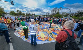 Die Demonstranten haben mitten auf der Herforder Straße ein großes buntes Tuch ausgebreitet und halten eine kurze Kundgebung ab. - Andreas Zobe