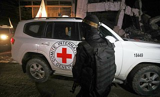 Ein bewaffneter Mann in der Uniform der al-Qassam-Brigaden, dem militärischen Flügel der Hamas, steht Wache, als Fahrzeuge des Roten Kreuzes ein Lagerhaus verlassen. In dem Lagerhaus sollen angeblich Särge mit den Leichen von vier verstorbenen Geiseln abgeholt und nach Israel gebracht werden. - Yousef Al Zanoun/AP/dpa
