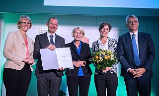 Preisverleihung:  Jürgen Krahl, Vorstandsvorsitzender der Stiftung Studienfonds OWL und Präsident der Technischen Hochschule OWL mit der Urkunde,  Ingeborg Schramm-Wölk, Vorstandsmitglied der Stiftung Studienfonds OWL und Präsidentin der Fachhochschule Bielefeld (Mitte) , Katja Urhahne, Geschäftsführerin der Stiftung Studienfonds OWL (2. v. r.), Bundesbildungsministerin Anja Karliczek (l.)  und Volker Meyer-Guckel, stellvertretender Generalsekretär des Stifterverbandes für die Deutsche Wissenschaft (r.). - BMBF/Hans-Joachim Rickel