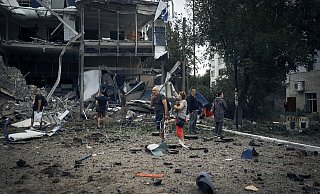 Ukraine: Menschen stehen, von Trümmern umgeben, vor zerstörten Gebäuden. - Kostiantyn Liberov/AP/dpa