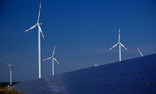 Windräder zur Stromerzeugung drehen sich in Mecklenburg-Vorpommern hinter einem Solarpark. - Foto: Jens Büttner/dpa-Zentralbild/dpa