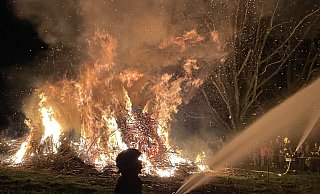 Wenn es auf Dembergs Hof in Bad Oeynhausen-Lohe stockdunkel ist, entzünden die Besucher ein mächtiges Osterfeuer. Damit die Flammen nicht auf die umliegenden Bäume übergreifen, halten Brandbekämpfer Wasserpistolen auf die Äste. - Elke Niedringhaus-Haasper