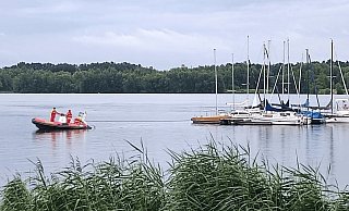 Ein DLRG-Motorboot schleppt den abgetriebenen Steg mit insgesamt acht festgebundenen Booten zurück ans Ufer. - DLRG