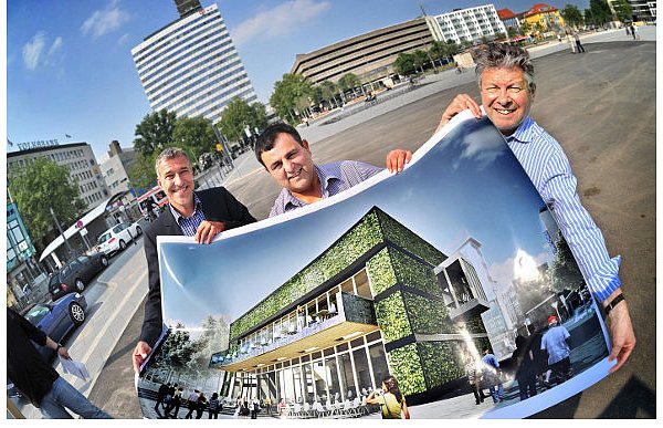 BGW-Projektplaner Jörg Höfel, Gatronom Beyhan Polat und BGW-Geschäftsführer Norbert Müller (v.l.) zeigen den Würfel-Bau mit Balkon und Terrasse, der bald auf der noch asphaltierten Fläche, auf der sie stehen, gebaut wird. - © FOTO: ANDREAS FRÜCHT