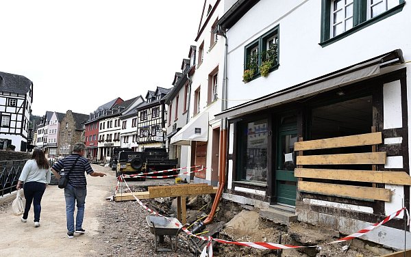 Passanten gehen in Bad Münstereifel über eine Straße, an der einen Monat nach der Hochwasserkatastrophe die Wiederaufbau begonnen hat. - © picture alliance/dpa
