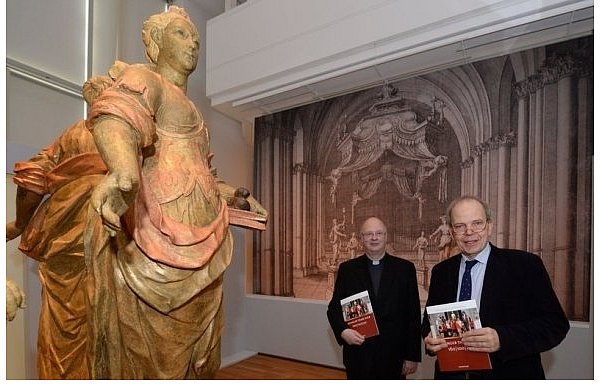 Der Generalvikar des Erzbistums Paderborn, Alfons Hardt (r.), und Dr. Christoph Stiegemann, Direktor des Diözesanmuseums, halten die Infobroschüre in ihren Händen. Im Vordergrund ist eine von vier überlebensgroßen allegorischen Figuren zu sehen, die einst im Dom den Liborischrein umgaben. - © FOTO: MARC KÖPPELMANN