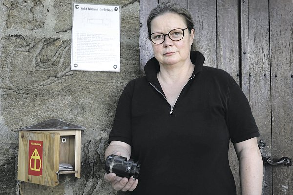 Nicht mehr zu gebrauchen: Pfarrerin Barbara Fischer hält den völlig zerstörten Pilgerstempel in der Hand, der in einem kleinen Kästchen neben dem Eingang zum Turmraum aufbewahrt wird. - © Cornelia Müller