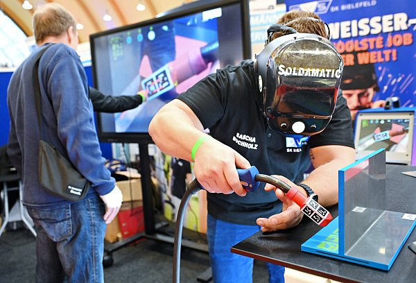 Sascha Buchholz von der "schweißtechnischen Kursstätte Bielefeld" zeigt, wie virtuell geschweißt wird. Hinten auf dem Bildschirm sehen die Zuschauer seine Arbeit. - © Barbara Franke