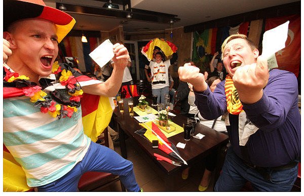 Sven Babér (l.) und Ramon Horrocks jubeln nach dem 1:0 mit ihren Tippscheinen im Café Solero an der Herforder Straße. Zu diesem Zeitpunkt können beide Fußballfans mit ihren Tipps noch richtig liegen. - © FOTO:JOHANNES WÖPKEMEIER