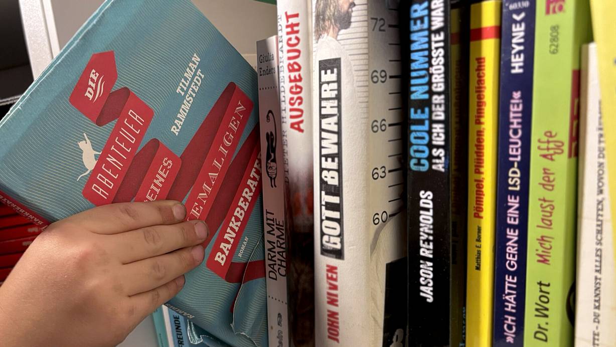 Der Roman "Die Abenteuer meines ehemaligen Bankberaters" von Tilmann Rammstedt wird aus einem heimischen Bücherregal gezogen. | © Katharina Eisele