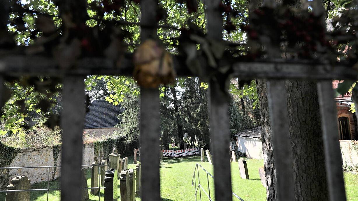 Ein Blick durch das Eingangstor, an dem eine verwelkte Rose hängt, zum Jüdischen Friedhof in Warburg. | © Simone Flörke