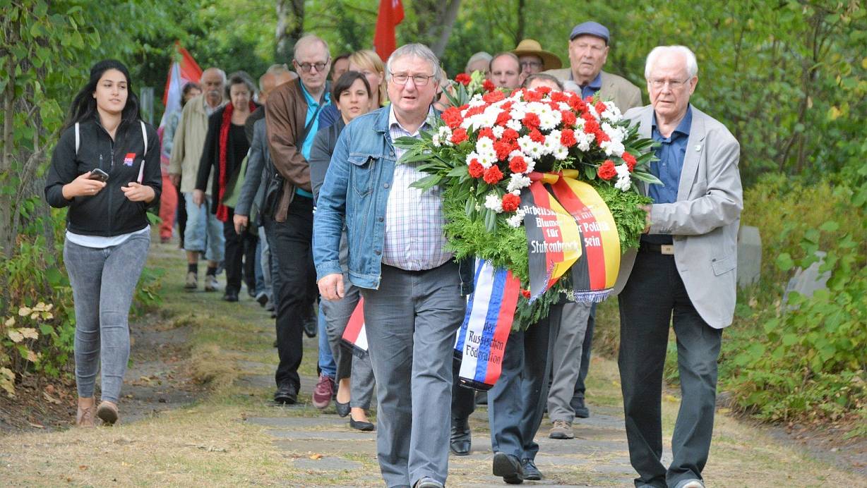 Feierlich: Hubert Kniesburges, Vorsitzender des Arbeitskreises „Blumen für Stukenbrock“ (vorne l.) und sein Vorgänger Werner Höner fuhren den langen Zug an und tragen einen der Kränze, die am Obelisken niedergelegt werden. | © Karin Prignitz