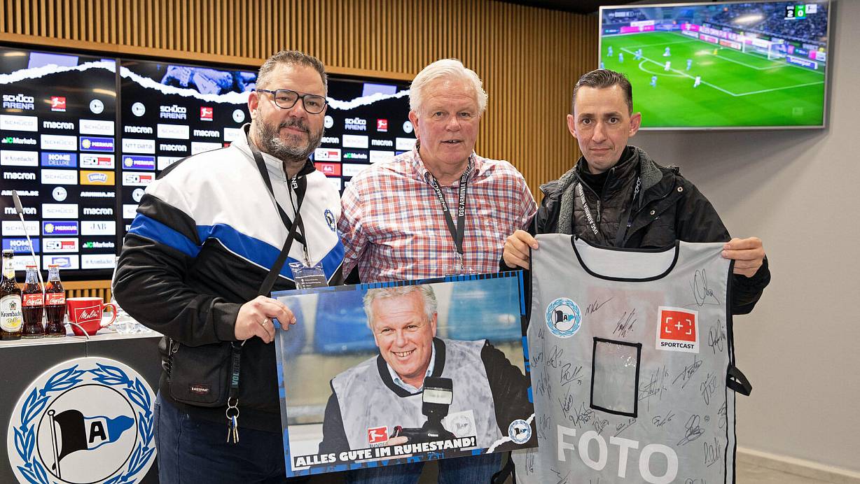 Für Wolfgang Rudolf (M.) war das 2:2 gegen Wolfsburg das letzte Arminia-Heimspiel seiner langen Berufskarriere. Arminia-Sprecher Daniel Mucha (l.) und DSC-Fotograf Thomas F. Starke (r.) verabschiedeten ihn mit einem vom Team signierten Foto-Leibchen. | © Foto: Friso Gentsch