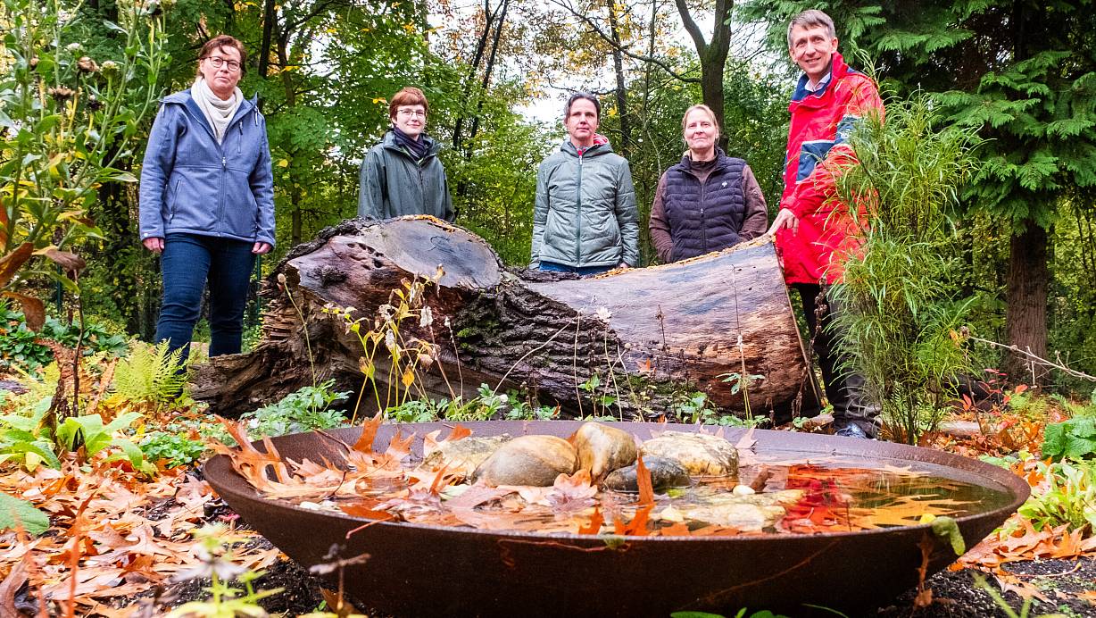 Friedhofsleiterin Anke Schröder (v. l.), Friedhofsgärtnerin Elisabeth Goll, Schöpfungsbotschafterin Karen Schröer, Gärtnermeisterin Kathrin Eichholz und Marien-Pfarrer Gerald Wagner hoffen, dass das ökologische Gräberfeld gut angenommen wird. Die Wasserschale ist für Tiere gedacht, der Totholzstamm für Insekten – und auch das Laub darf liegenbleiben. | © Ralf Bittner