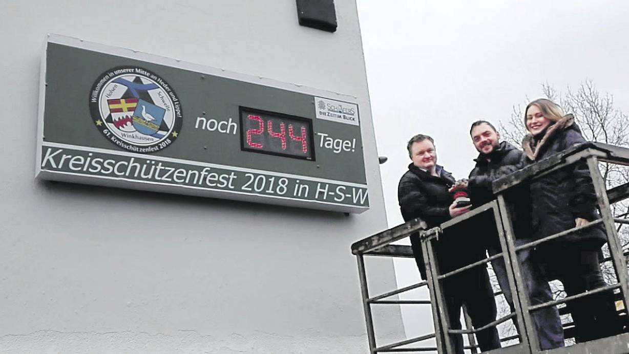 Countdown: (v. l.) Holsens Ortsvorsteher Christian Heber und das Kreiskönigspaar Henning Gurk und Denise Brosien an der Anzeige. |