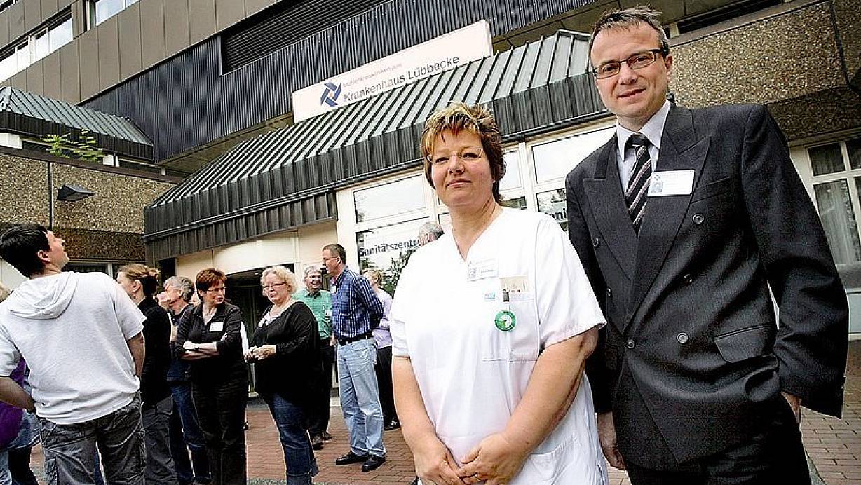 Krankenschwester Andrea Schürmann (l.) hat für ihre Patienten weniger Zeit. Geschäftsführer Mario Hartmann behält den wirtschaftlichen Erfolg und das Wachstum des Krankenhauses im Auge. Hinter ihnen stellen sich andere Mitarbeiter für ein Gruppenfoto zum Jubiläum auf. | © FOTO: TYL