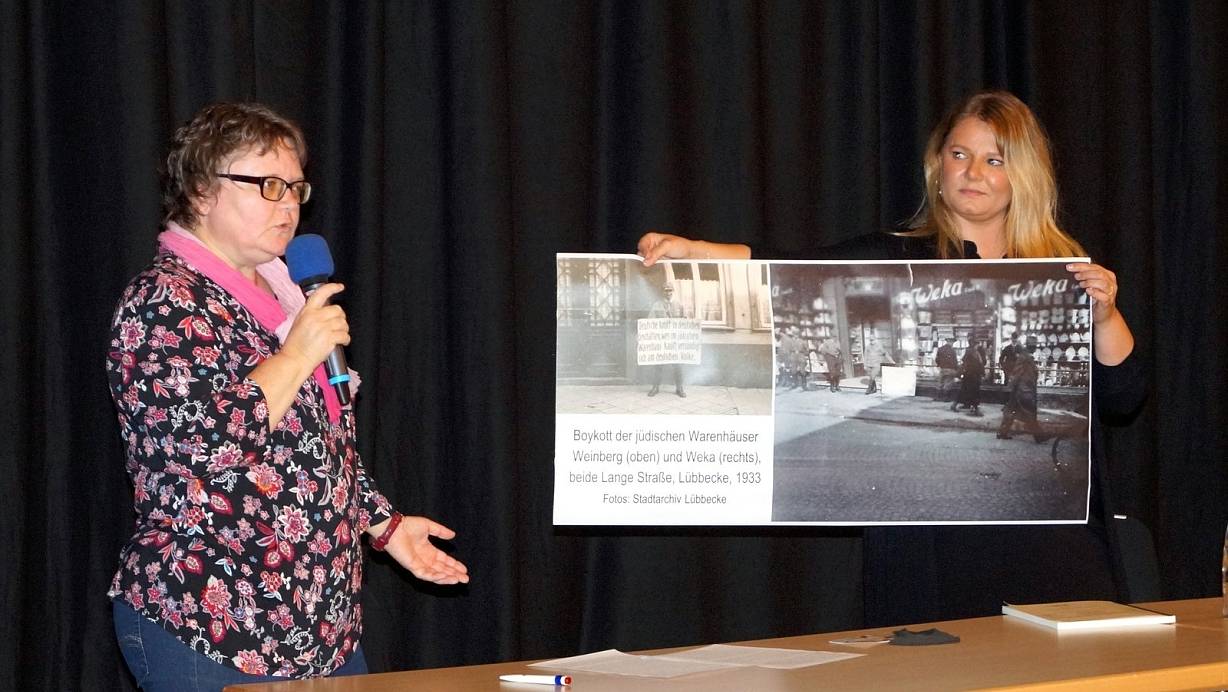 Stadtarchivarin Christel Droste (l.) und Nina Pape (Geellschaft für Christlich-Jüdische Zusammenarbeit in Minden) zeigen ein Foto vom Boykott jüdischer Kaufhäuser während der Nazizeit. | © Michael Grundmeier