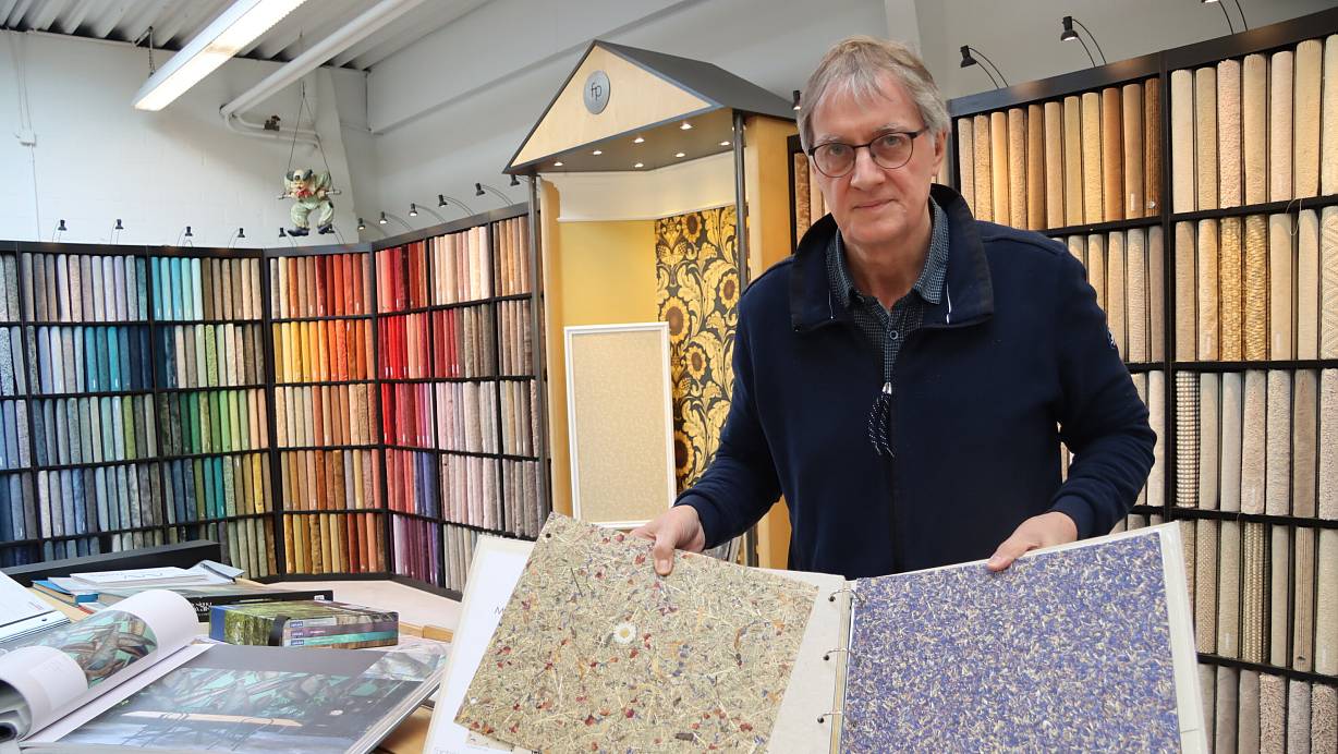 Gert Prüßner steht in seinem Teppichboden-Studio und blättert am Kollektions-Tisch durch verschiedene Tapetenmotive. Neben den beliebten Digitaldruck-Fototapeten sind besonders die duftenden Varianten aus Österreich ein echter Hingucker – ihre Oberflächen bestehen aus getrocknetem Heu oder Kornblumen. | © Anna Lena Hinder