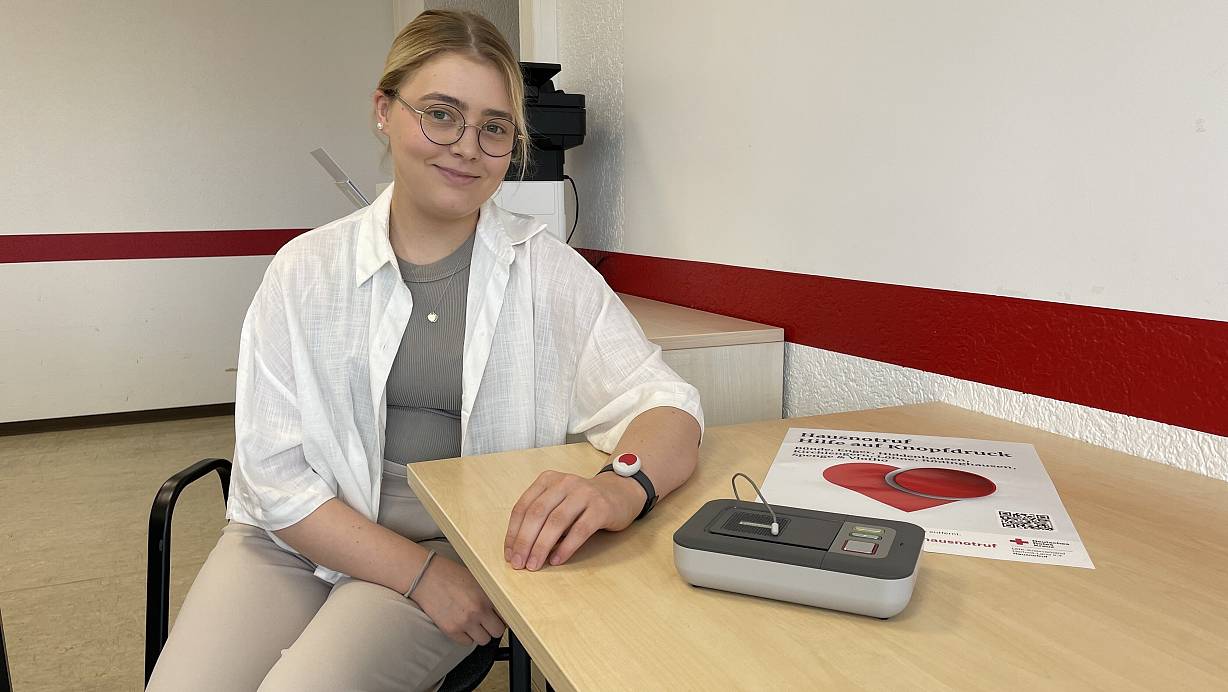 Ein Armband mit Notruf-Knopf und eine Basisstation: Franziska Fronzeck vom DRK Herford-Land demonstriert das neue Angebot des Kreisverbandes. | © Shannon-Lee Bendig