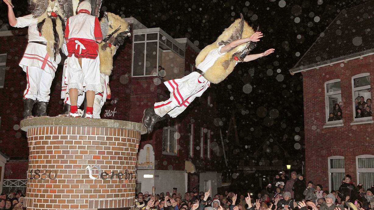 Mit Masken verkleidete Männer des Vereins "Borkumer Jungens" stürzen sich am Abend (Archivfoto aus dem Jahr 2011) in der Innenstadt der Nordseeinsel von einer Säule in die Arme der Schaulustigen. | © Reinhold Grigoleit/picture alliance/dpa