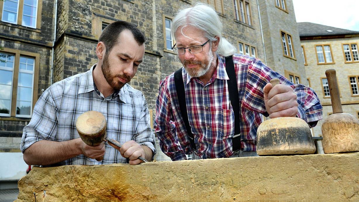 Sehr gut zu bearbeiten: Der Steinbildhauer Heinz-Werner Horn (rechts) und Geselle Konstantin Hadt am Osningsandstein. Im Hintergrund das Ratsgymnasium. | © Barbara Franke