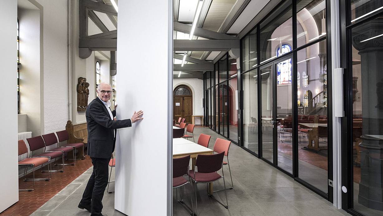 Pfarrer Christoph Steffen demonstriert, wie man mit Hilfe einer Trennwand mehrere Räume unter der Empore erhält. | © Jörg Dieckmann -www.dieckmann-fotodesign.de