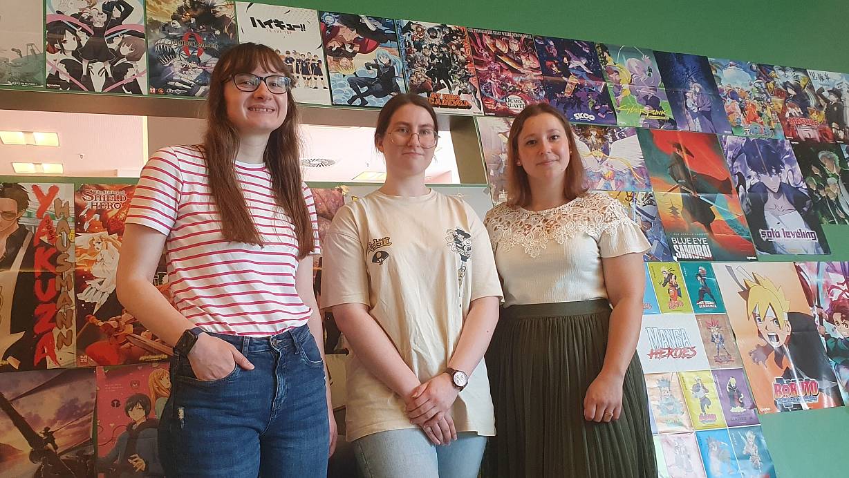 Startklar für den Manga Day: die Azubis Julia Rathert und Lara Pietsch mit Veranstaltungskauffrau Natalia Baron (v.l.) vor einen bunten Manga-Wand in der Bibliothek am Neumarkt. | © Heike Krüger