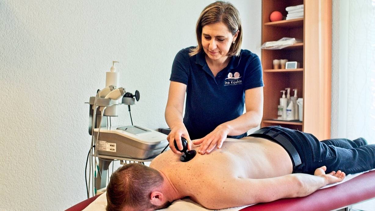 Ina Koshin (stehend) führt mit ihrem Kollegen Sergej Röhrig (liegend) die Anwendung der WINBACK Therapie vor. Der Körper wird über das Gerät bei der Behandlung stimuliert, der Patient fühlt eine leichte und entspannende Wärme. | © Wencke Meckenstock