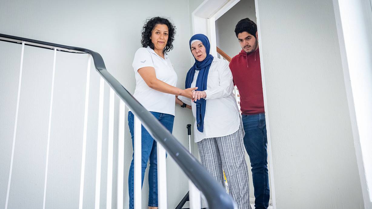 Für Dalila Mounajed (Mitte) sind die Treppenstufen vor ihrer Wohnung schier unüberwindliche Hindernisse. Selbst mit viel Hilfe durch ihre Physiotherapeutin Ahu Hankl (links) und Sohn Karim (22, rechts) traut sie sich nur selten hinunter oder hinauf. | © Sarah Jonek Fotografie