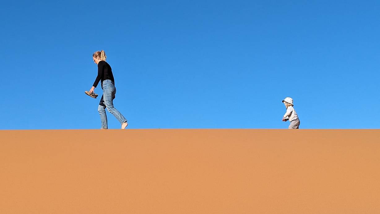 Angekommen im größten Sandkasten der Welt, der Sahara: Mutter und Kind spazieren vor leuchtend blauem Himmel durch die Dünen. | © privat