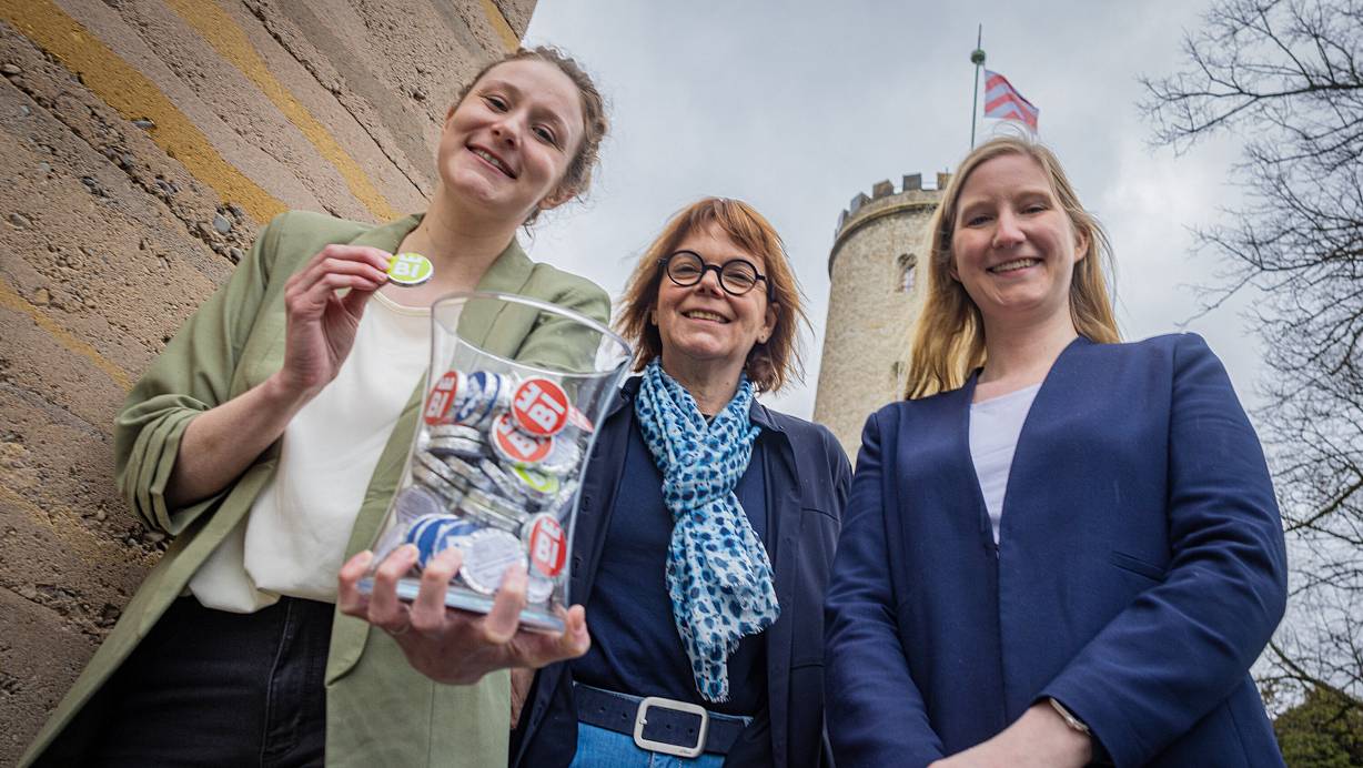 Mit der flatternden Burgfahne über den Köpfen: Jill Mallin (von links), Gabriela Lamm und Jacqueline Heger von Bielefeld Marketing werben mit Bi-Schoko-Talern für ihre Freizeitangebote. | © Mike-Dennis Mller / www.mdm.photo