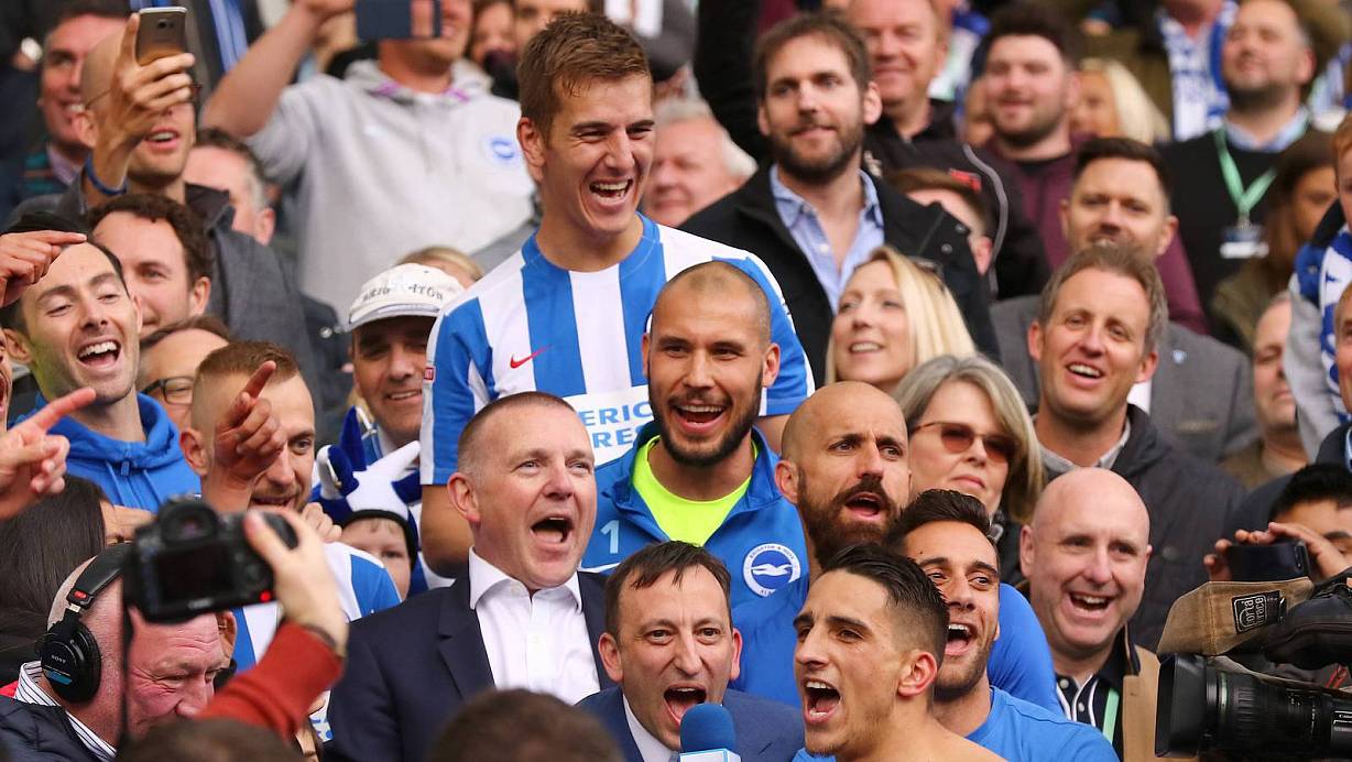 So feiern Aufsteiger: Uwe Hünemeier (oben) feiert mit Fans und Teamkollegen auf der Tribüne des Amex-Stadions. Brightons Vereinspräsident Tony Bloom, dessen Investitionen den Erfolg erst ermöglicht hatten, betätigt sich unterdessen als Vorsänger am Mikro. | © Imago/Mark Kerton