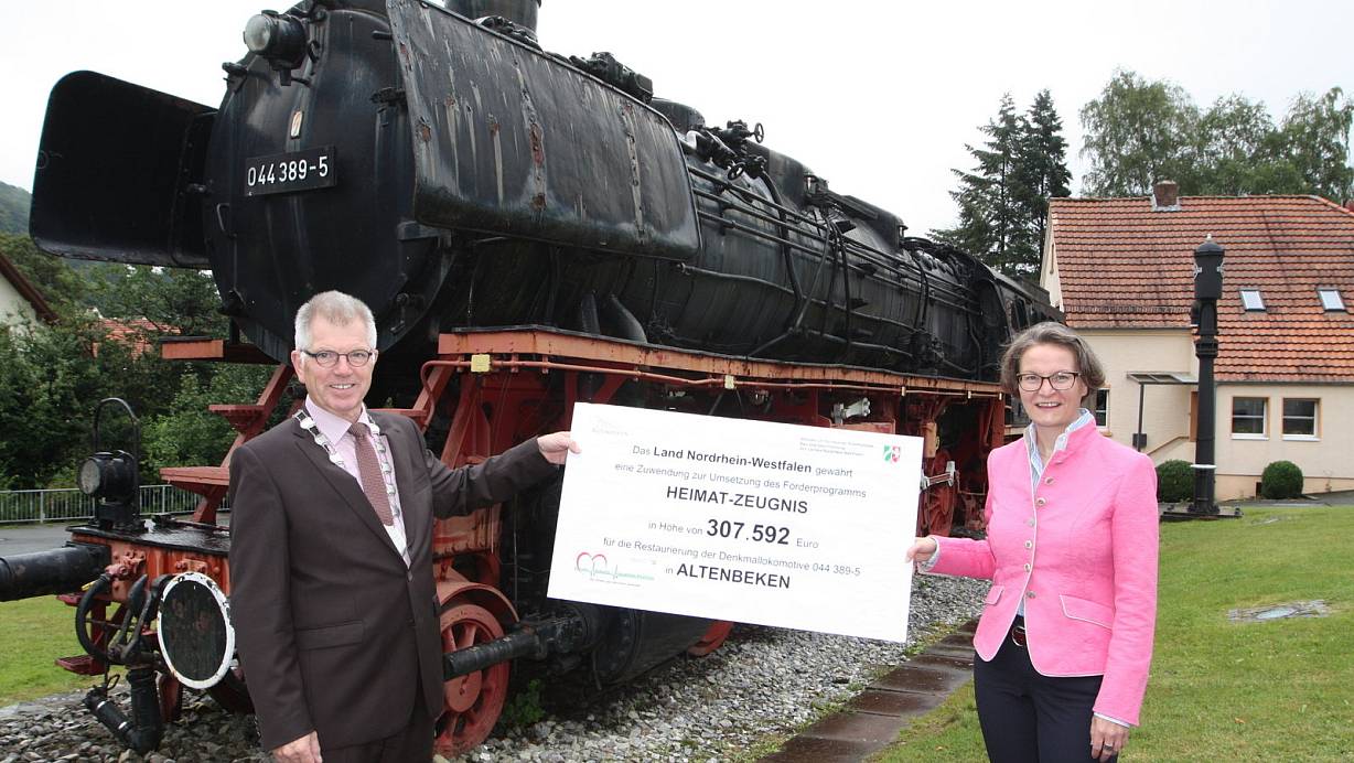 Ina Scharrenbach, NRW-Ministerin für Heimat, Kommunales, Bauen und Gleichstellung, übergibt Altenbekens Bürgermeister Hans Jürgen Wessels den großen Scheck für die Restaurierung der fast 80 Jahre alten Dampflokomotive. | © Uwe Müller