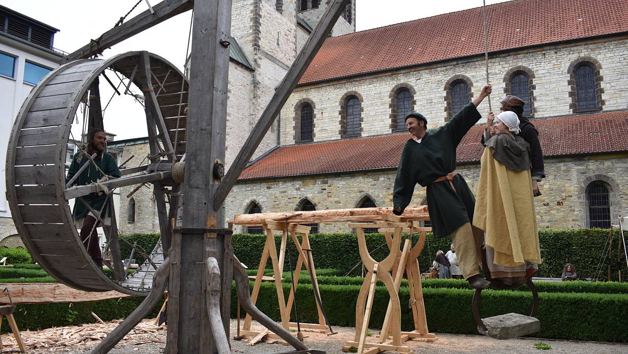 Stark: Nur mit der Kraft seiner Beine hebt Florian Westphal (im Laufrad) hier rund 250 Kilogramm. Durch die Umdrehungen des Laufrads wickelt sich das Seil um eine Welle, so wird der Greifarm des mittelalterlichen Krans hoch und auch wieder herunter bewegt. | © Svenja Ludwig