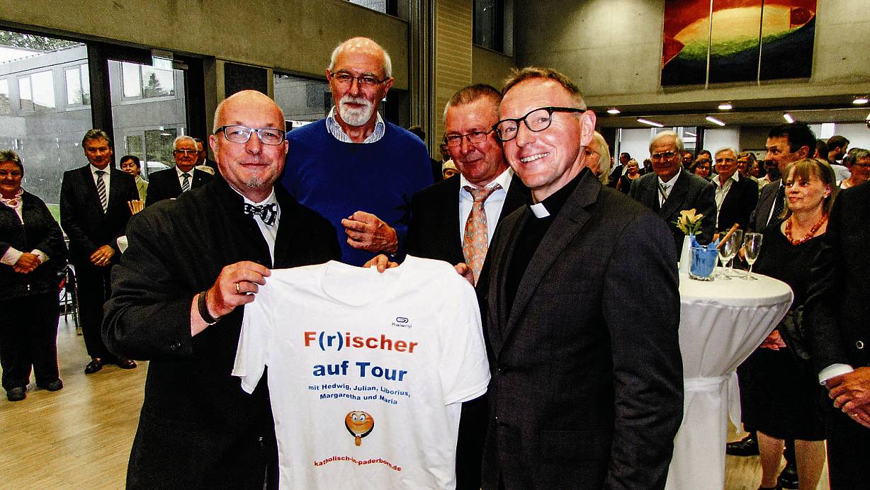 F(r)ischer auf Tour: (v .l.) Heribert Zelder (Moderator des Empfanges), Franz Steffenvauseweh (Vorsitzender der Pfarrgemeinde Sankt Liborius) und Horst Steinhoff (Vorsitzender der Pfarrgemeinde St.Julian) schenkten Benedikt Fischer ein T-Shirt zum Joggen. | © Jana Tessaring