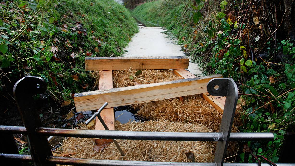 Die Ölsperre: Mit einem Bindemittel – erkennbar als heller Film hinter den Strohballen – wurde am vergangenen Donnerstag das Öl auf dem Wasser des Grabens am Kapellenweg abgestreut. Welcher Stoff genau von dem benachbarten Unternehmen eingeleitet worden ist, muss jetzt ein Labor herausfinden. Ob es sich bei der Verunreinigung um einen Unfall oder eine Straftat handelt, ermittelt die Polizei. Fest steht: Bereits zehn Tage zuvor hatte es erste Hinweise auf eine Einleitung gegeben. | © Roland Thöring