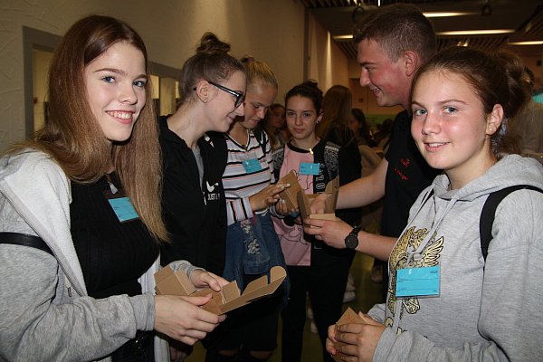 Azubi Dennis Metzger vom Verpackungsunternehmen Wellteam zeigt Löhner Schülerinnen, wie sie den Karton falten müssen. - © Anthea Moschner