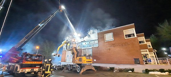 Während ein großer Bagger mit Greifer Teile des verkohlten Daches der Nieheimer Sparkasse herunterholt, wird das Feuer von Drehleitern aus gelöscht. - © David Schellenberg