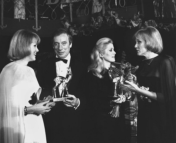 16. Januar 1976, München: Die französische Schauspielerin Catherine Deneuve und ihr Landsmann Yves Montand, die je einen Bambi für ihre Rollen in dem Film "Die schönen Wilden" erhalten haben, im Gespräch mit Alice (l.) und Ellen Kessler. - © Istvan Bajzat/dpa