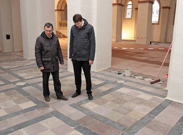 Pfarrer Eckhard Düker (l.) und Kantor Tim Gärtner sehen sich im Seitenschiff der Paderborner Abdinghofkirche den Fußboden an, dessen historisches Muster wieder erkennbar geworden ist. - © EKP/Oliver Claes