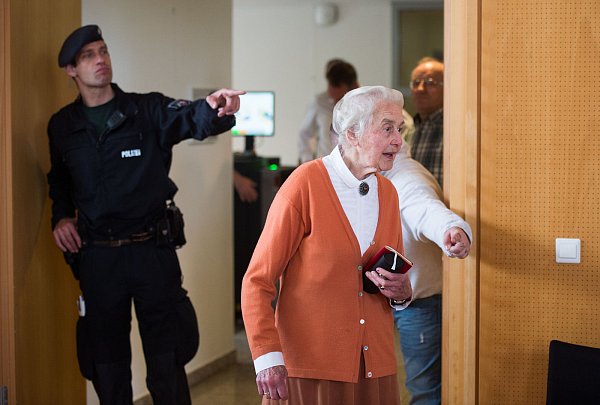 Dort geht es lang: Ein Polizeibeamter weist Ursula Haverbeck-Wetzel den Weg zu ihrem nummerierten Zuschauerplatz. - © dpa