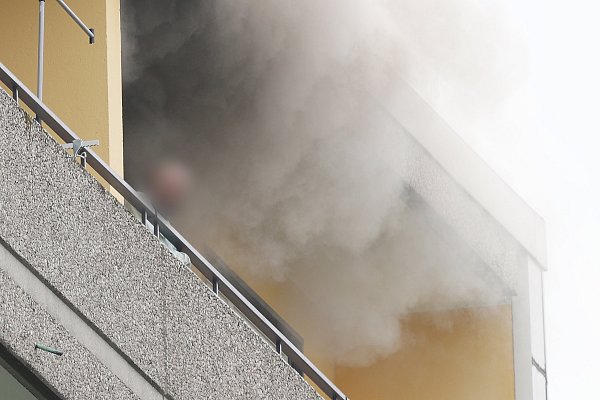 Eine Person steht auf dem Balkon des Hochhauses. Rauch quillt hervor. - © David Young