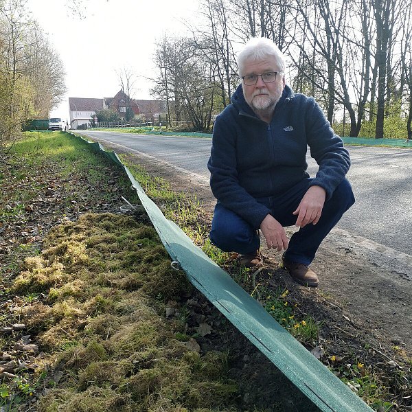 Dirk Rosenlicht (NABU Leopoldshöhe) im vergangenen Jahr an einem der Amphibienzäune an der Eckendorfer Straße. Im Hintergrund ist ein Teil des Gut Eckendorf sichtbar. Hinter dem Zaun ist Moos gelagert, das die Ehrenamtlichen in die Eimer packen, in die die Amphibien fallen. - © Straßen NRW