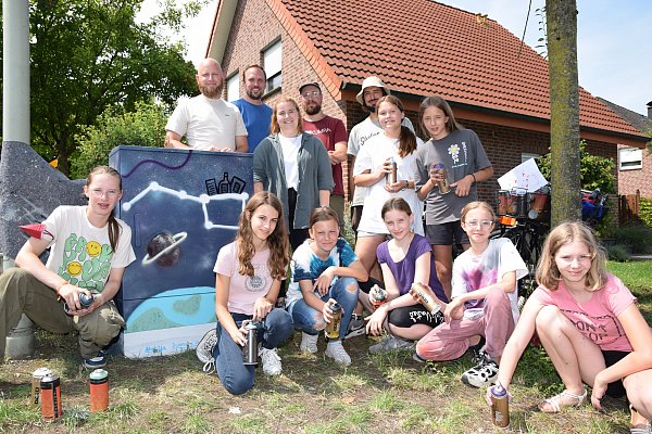 Manuel Begenat (Stadt), Benjamin Ludwig (Droste-Haus), Pauline Meckes (Stadt), die Graffiti-Künstler Lukas Kröger und Nils Neumeyer sowie die Jugendlichen Amelie Schweda und Nele Manthei (hinten v. l.), Matilda Kleinerüschkamp, Sookie Westerbarkey, Leonie Hartkämper, Lea Schniedertöns, Lina Jolien Rehpöhler und Isabell Thiessen (vorne v. l.) vor einem der gestalteten Stromkästen am Rebhuhnweg. - © Karin Prignitz